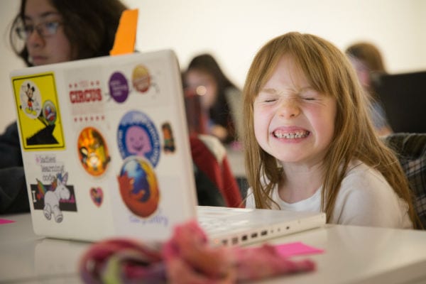 Young girl with laptop smiling at Girls Learning Code summer camp