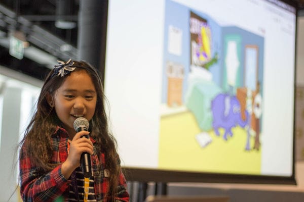 Young girl with microphone presenting in front of projection screen at Girls Learning Code summer camp