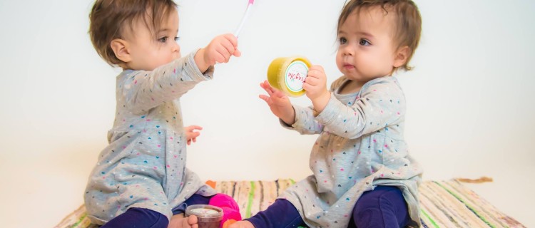 two babies playing with spoon and Fragola brand baby food container