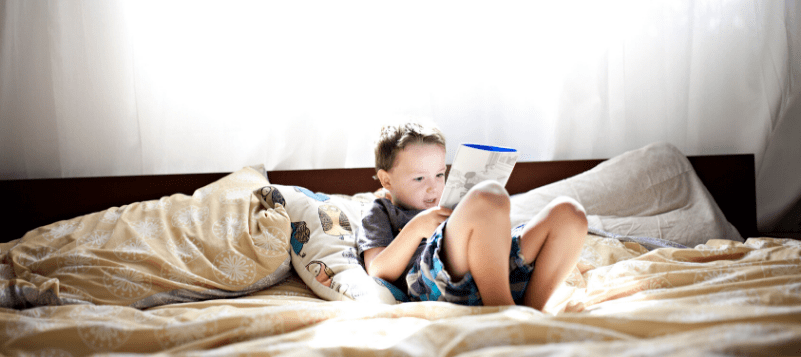 Young boy reading book in bed