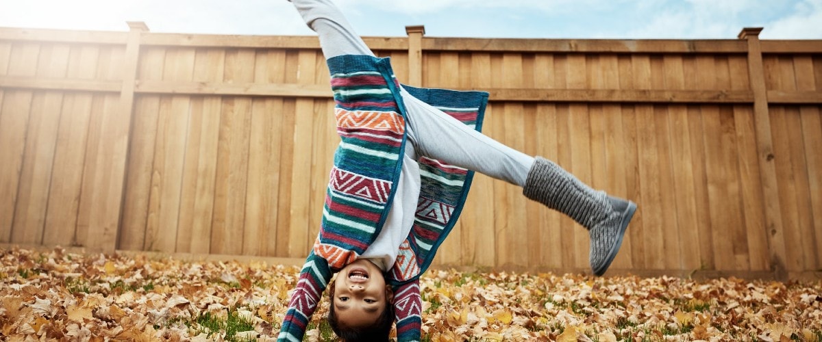 child doing cartwheel in leaves during fall