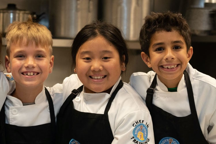 three kids in Rooks to Cooks chef uniforms smiling at camera