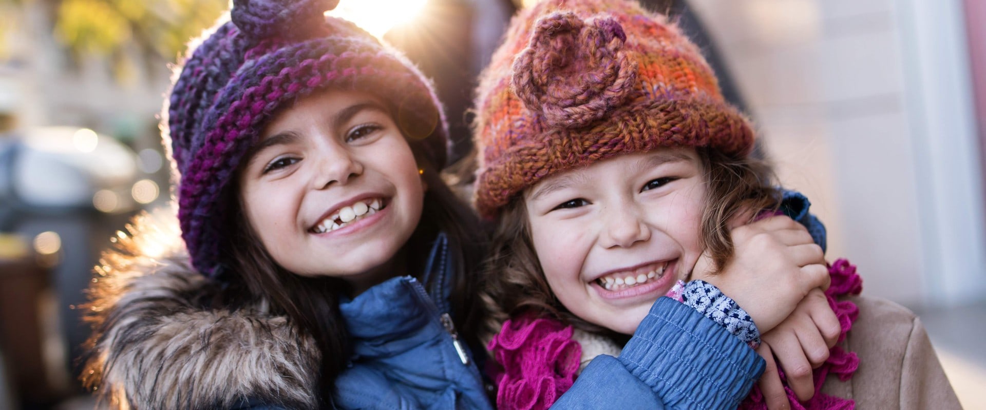 Sisters hugging and smiling at camera in winter on city street