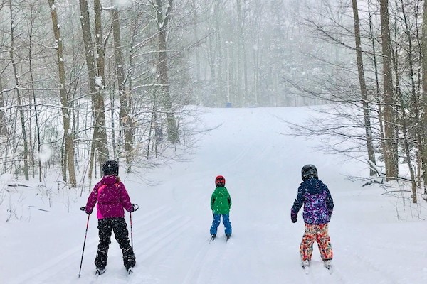 Shot from behind of three kids skiing in winter at Glen Eden, Ontario