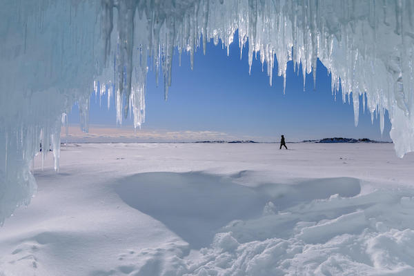 View onto snowy landscape and person cross-country skiing in distance from inside an ice cave at Copper Mine Point on Lake Superior, Ontario