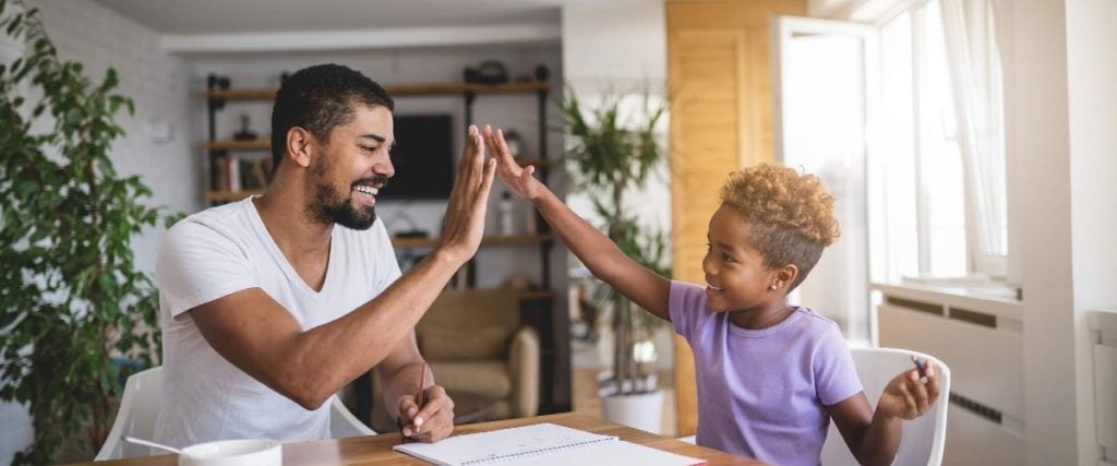 dad and child high-five over kitchen table with homework