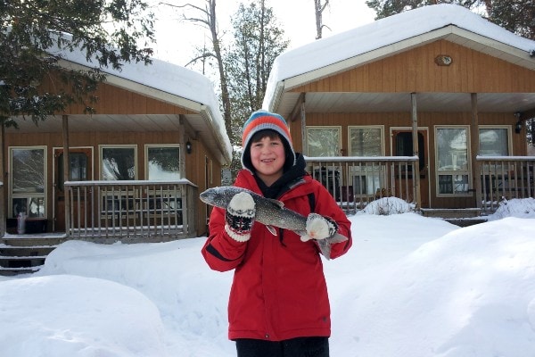 Boy holding freshly caught fish in front of Ogopogo Resort in winter