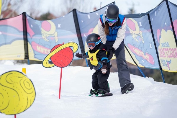 instructor helps preschool child learn to snowboard at Blue Mountain Resort
