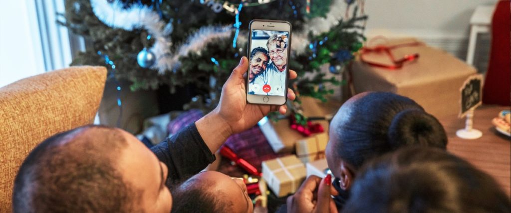 family talking to grandparents on video chat in living room in view of Christmas tree
